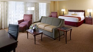 A hotel room with a bed, a sofa, a desk, two armchairs, and a small table with a vase of flowers.