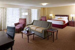 A hotel room with a bed, a sofa, a desk, two armchairs, and a small table with a vase of flowers.
