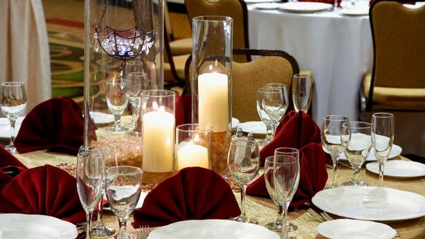 Une table de banquet dressée avec de l’argenterie blanche, des serviettes rouges et un grand arrangement floral en guise de centre de table.