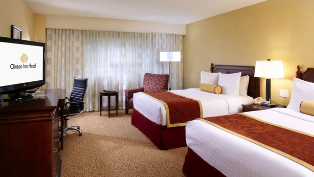A hotel room with two beds, a desk with a television, a chair, and a lamp.