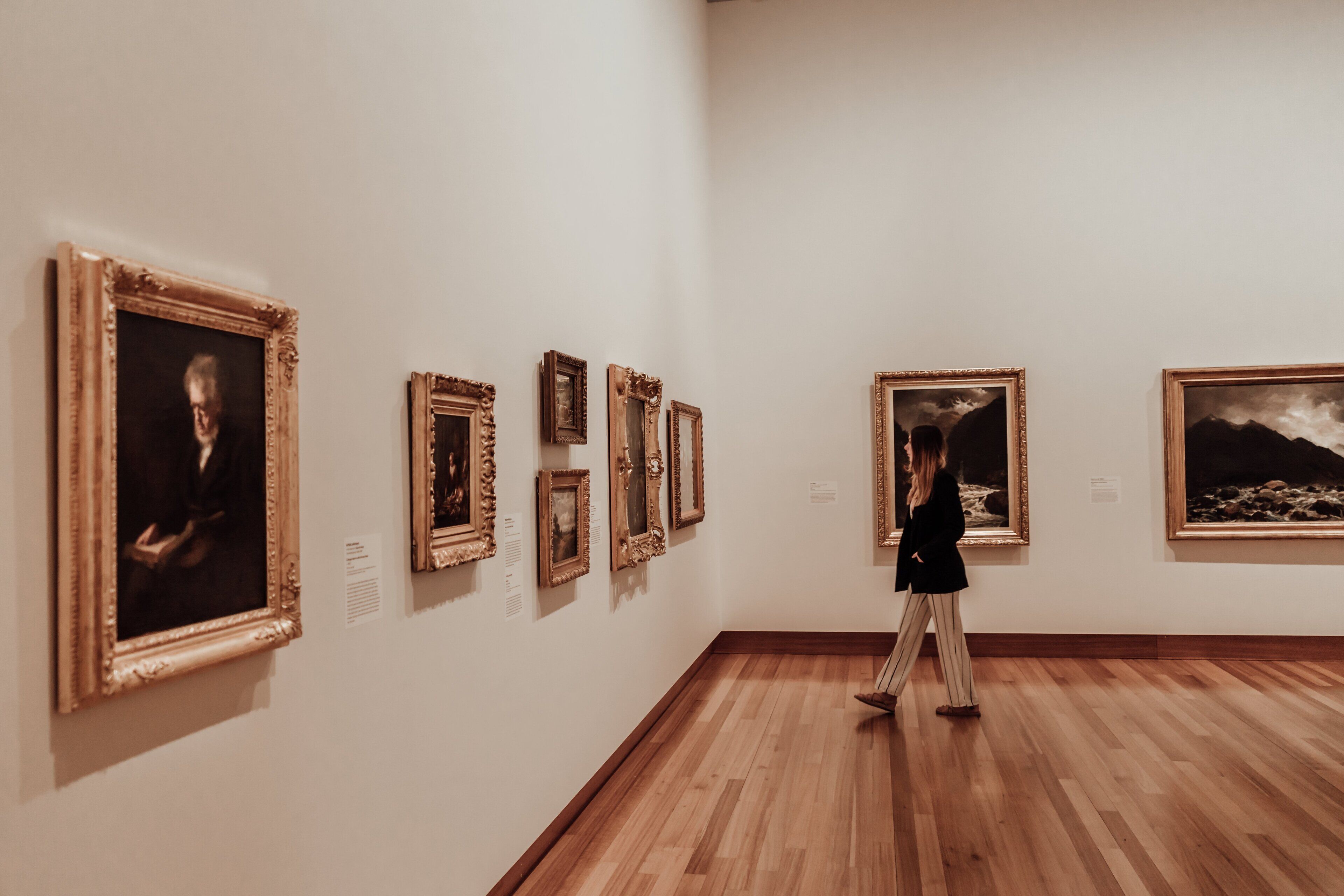 An art gallery with wooden floors and white walls, displaying framed artworks.