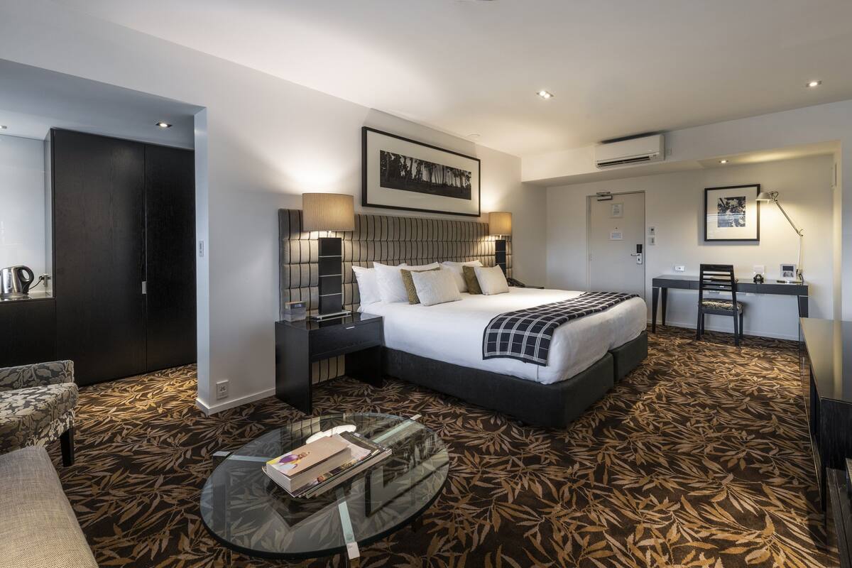 A modern hotel room with a large bed, a desk, a chair, a sofa, and a coffee table.
