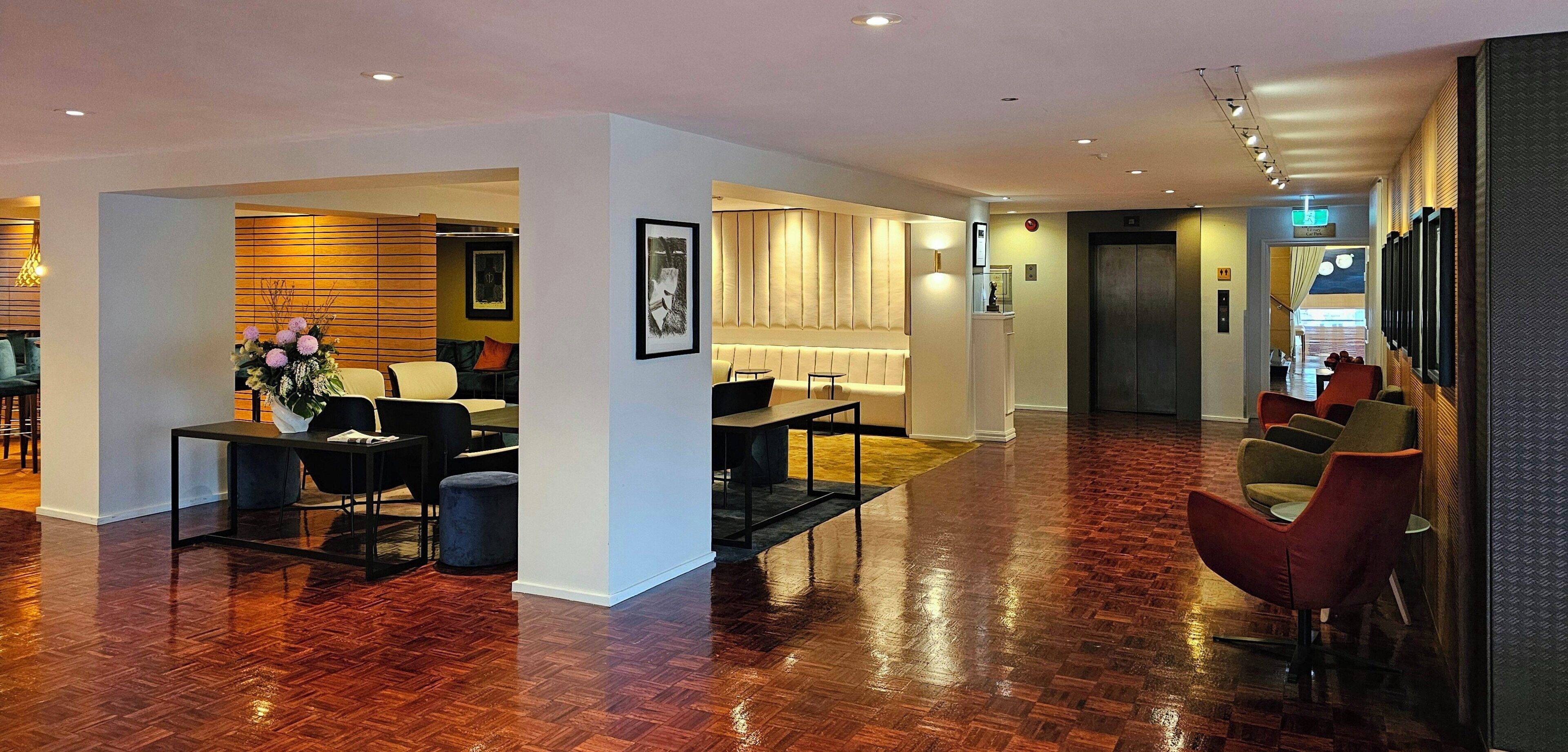 A spacious lobby with a wooden floor, seating areas, and a reception desk.