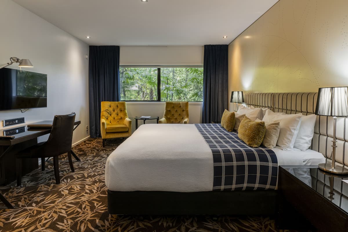 A hotel room with a large bed, a desk with a computer, a chair, and a TV on the wall.
