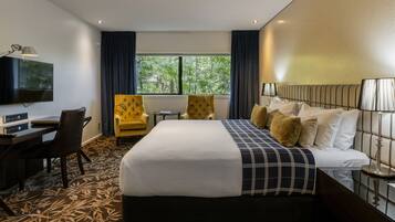 Quarto de hotel com uma cama grande, uma escrivaninha com computador, uma cadeira e televisão na parede.