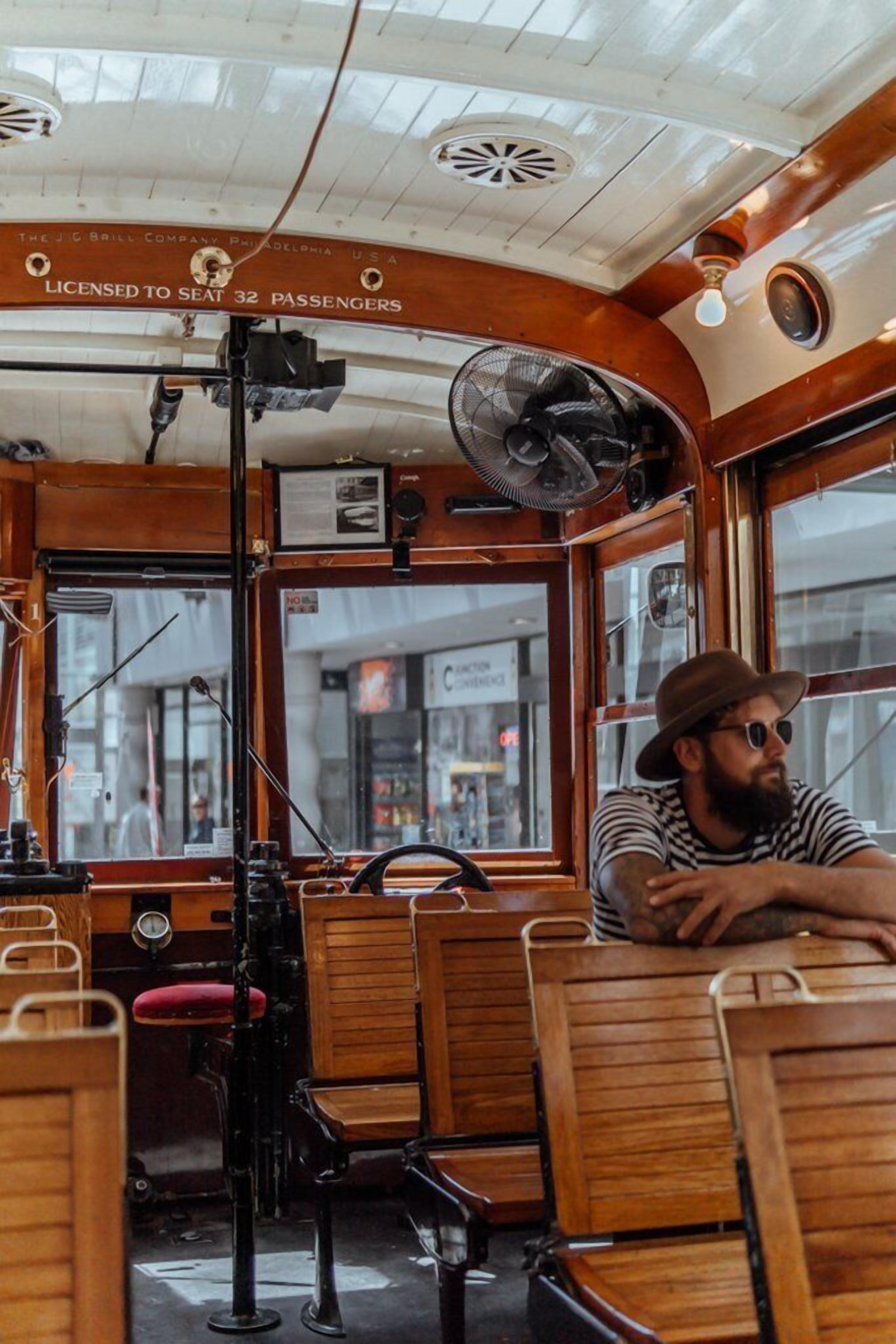 A vintage bus interior with wooden seats, a steering wheel, and a fan.
