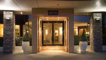 Step into The George's elegant entrance, featuring a glass door and a warm light fixture, surrounded by lush greenery and stone pillars.