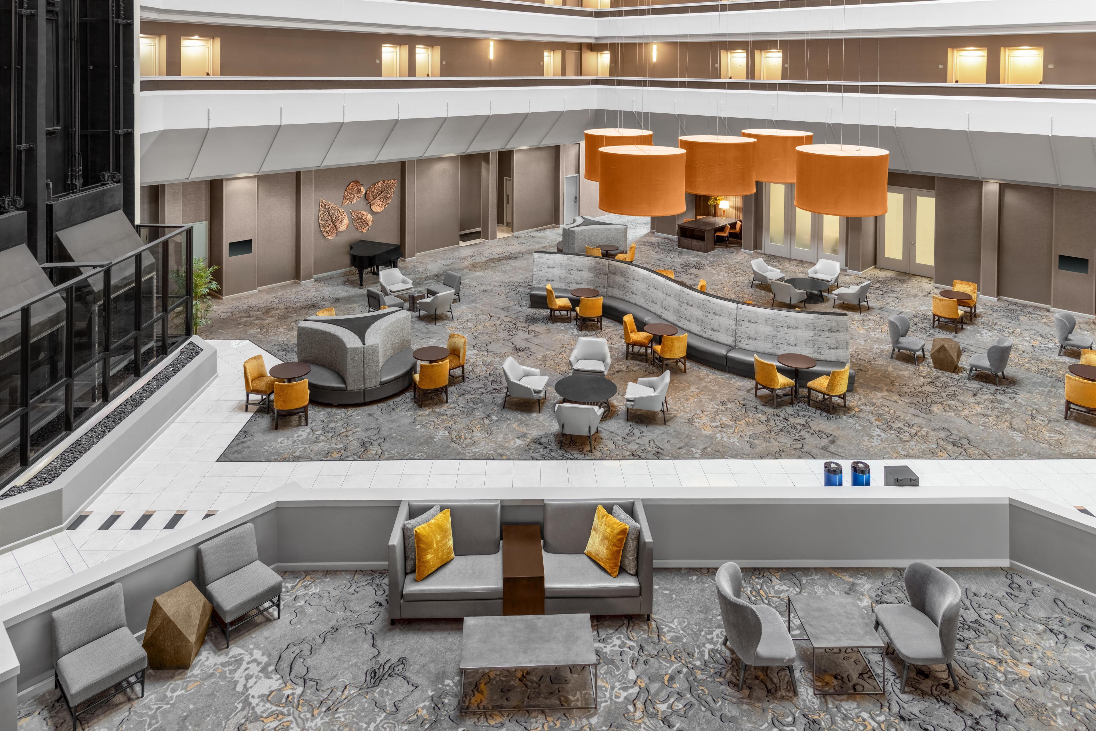 A spacious lobby with multiple seating areas, a piano, and a large wall with leaf decorations.
