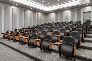A conference room with rows of chairs, carpeted floors, and a staircase leading to an upper level.