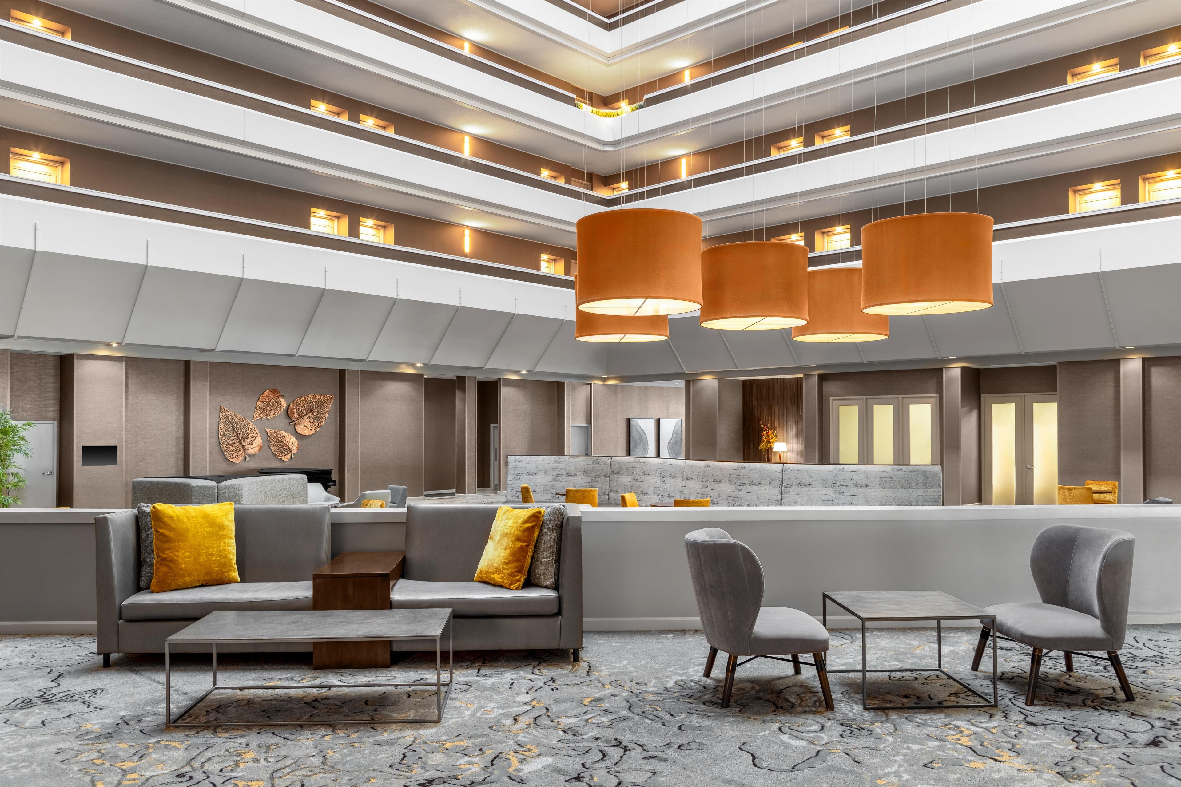 A modern hotel lobby with a seating area, a reception desk, and a high ceiling with lighting fixtures.