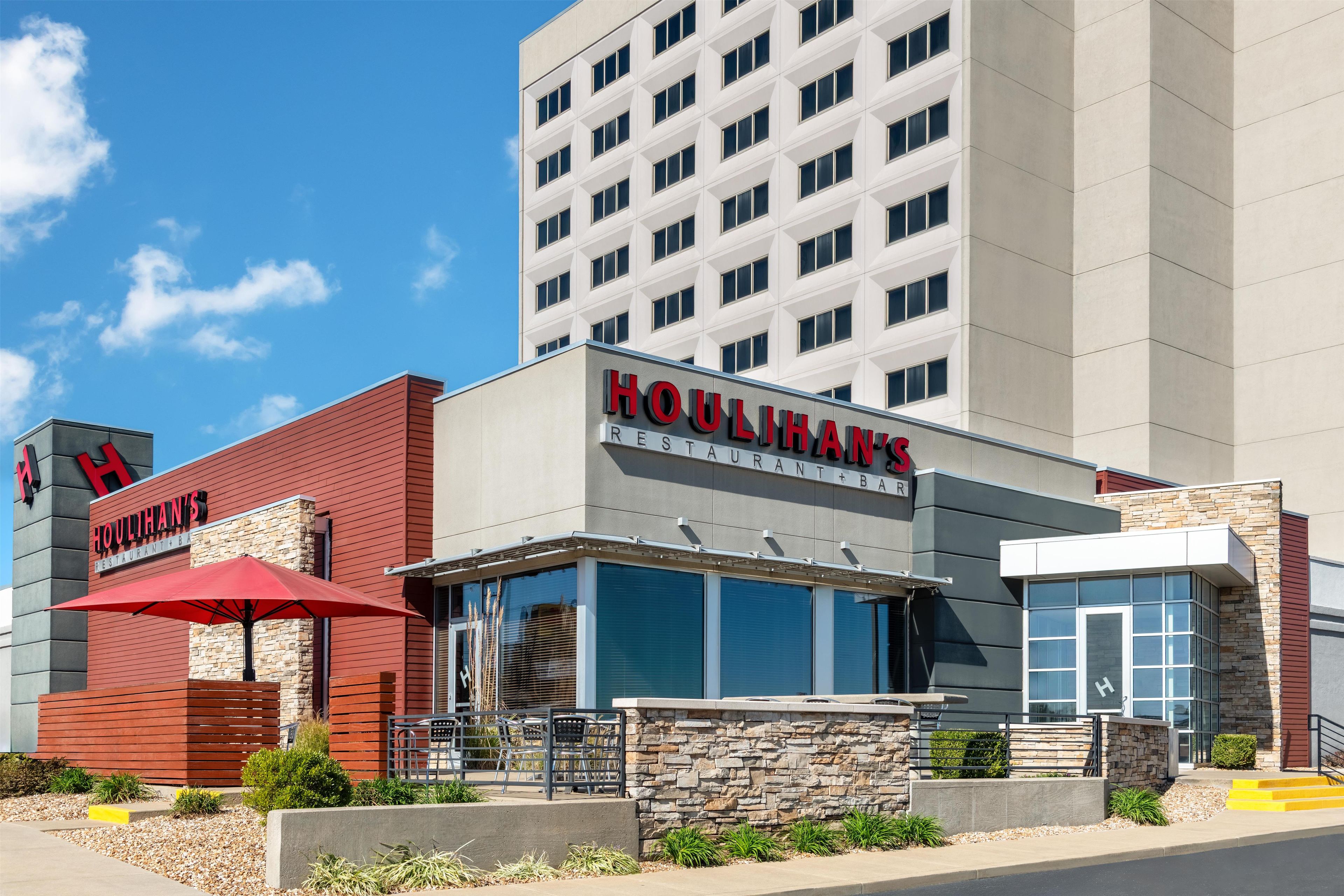 A hotel with a restaurant named 'Houlihan's' featuring a modern design with a red awning and stone facade.