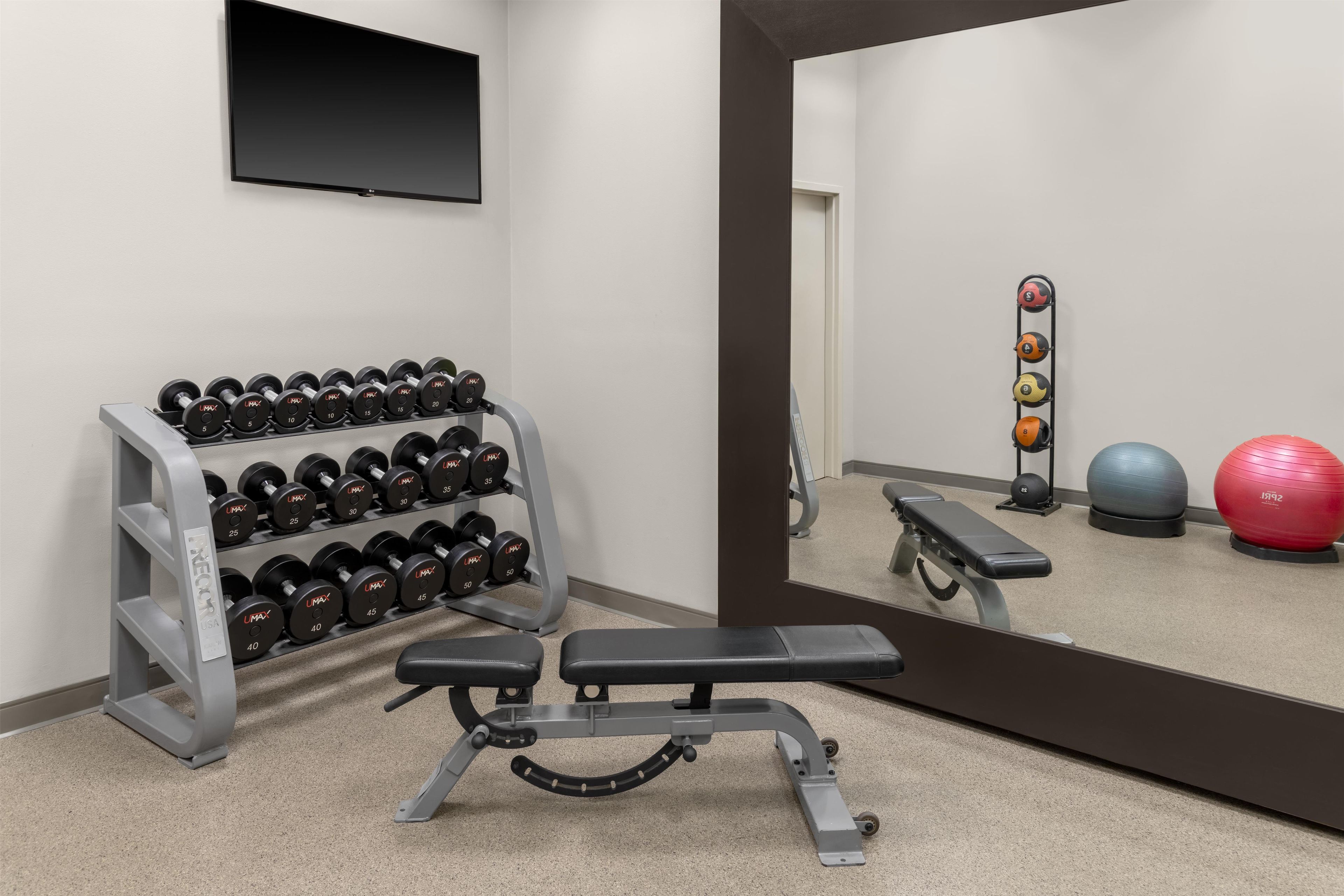 A gym with a bench press, a rack of dumbbells, a mirror, and exercise balls.