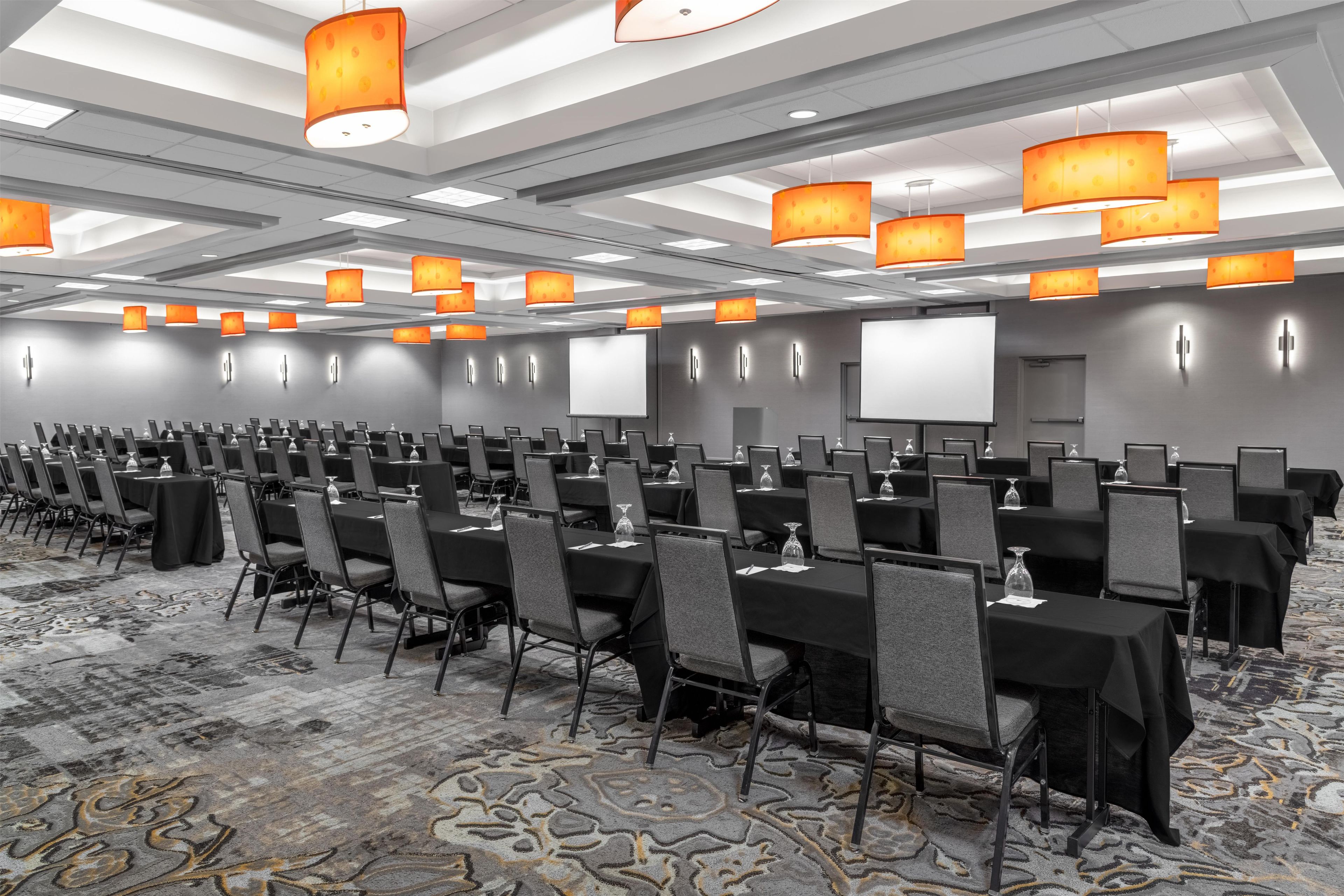 A conference room with rows of tables and chairs, equipped with projectors and screens.