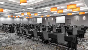 A conference room with rows of tables and chairs, equipped with projectors and screens.