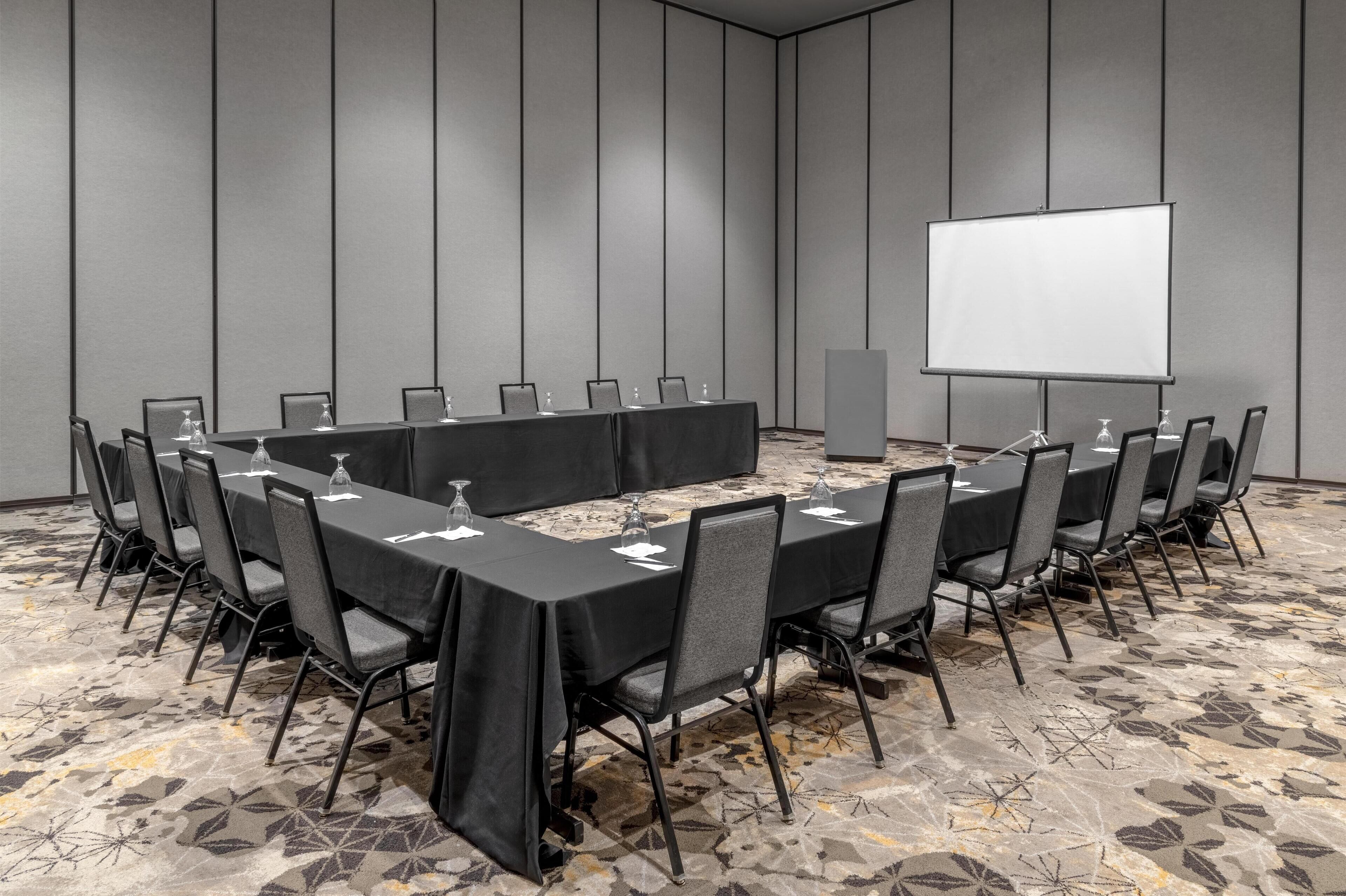 A conference room with a long table, chairs, a projector screen, and a carpeted floor.
