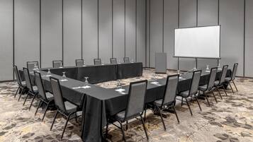 A conference room with a long table, chairs, a projector screen, and a carpeted floor.
