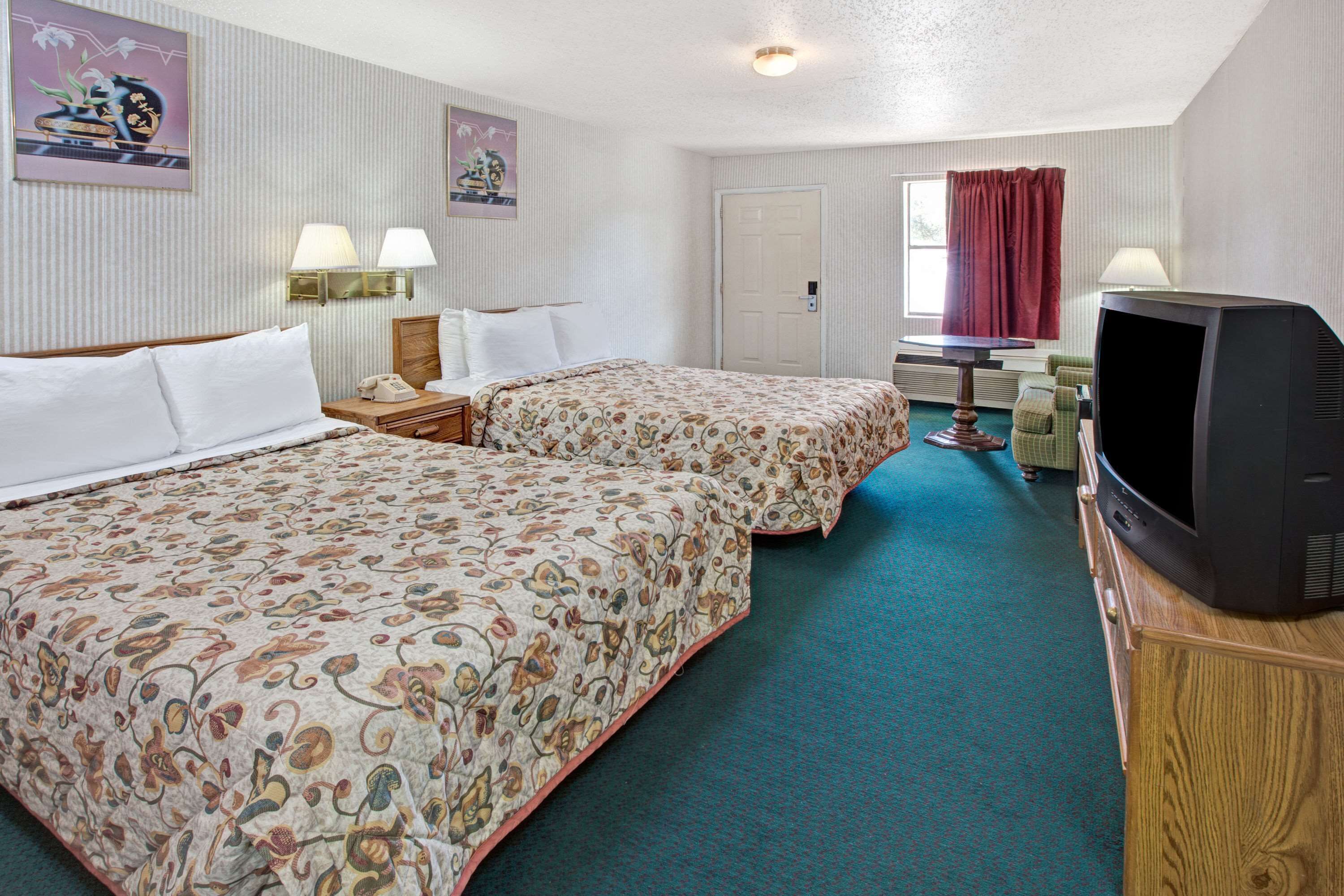 Habitación de hotel con dos camas, televisor, escritorio con lámpara y ventana con cortinas.