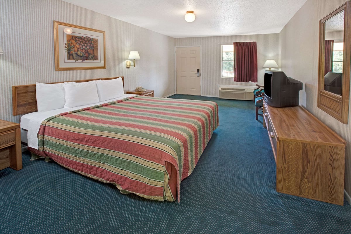 Een hotelkamer met een groot bed, een bureau met stoel, een televisie en een raam met gordijnen.
