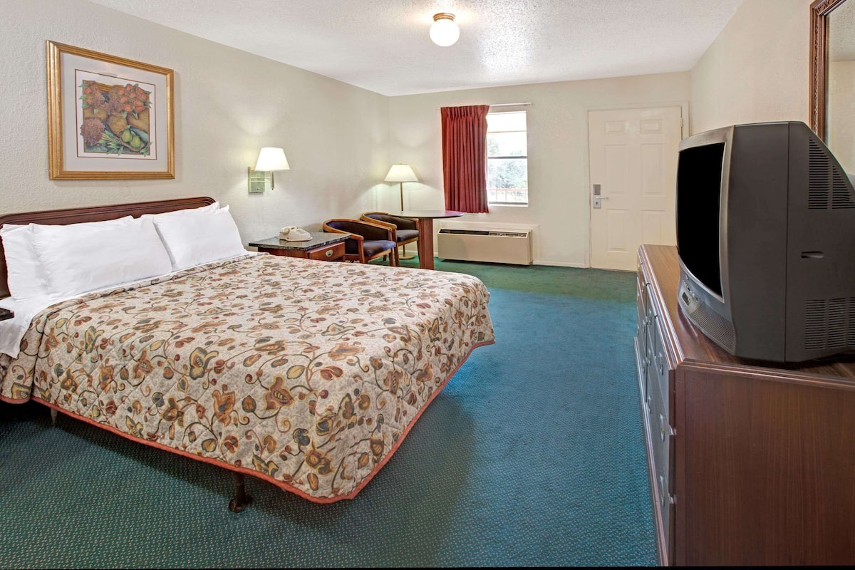 Een hotelkamer met een bed, een bureau, een stoel, een televisie en een raam met gordijnen.