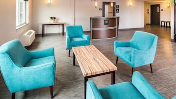 Un vestíbulo con sillas color turquesa, un mostrador de recepción, una mesa de madera y una planta en maceta.