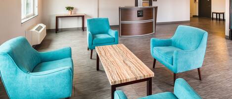 A lobby with teal chairs, a reception desk, a wooden table, and a potted plant.