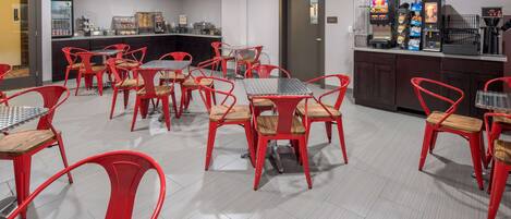 Un espace de restauration d'hôtel avec des chaises et des tables rouges, une machine à café et un présentoir réfrigéré.