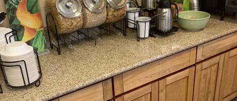 A kitchen counter with a coffee maker, a kettle, a bowl, and a sign that says "Fresh".