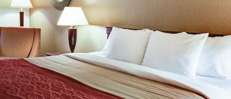 A hotel room with a neatly made bed, two bedside lamps, a round mirror on the wall, and a red patterned throw blanket.