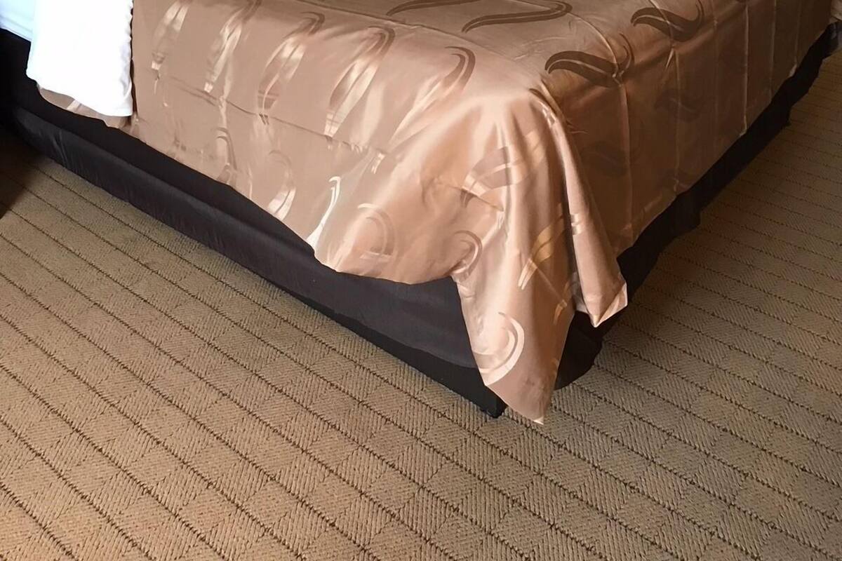 A neatly made bed with a brown patterned bedspread and white pillows, a bedside lamp, and two framed pictures on the wall.