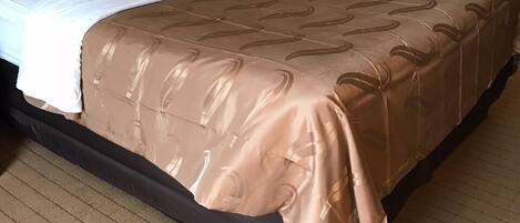 A neatly made bed with a brown patterned bedspread and white pillows, a bedside lamp, and two framed pictures on the wall.
