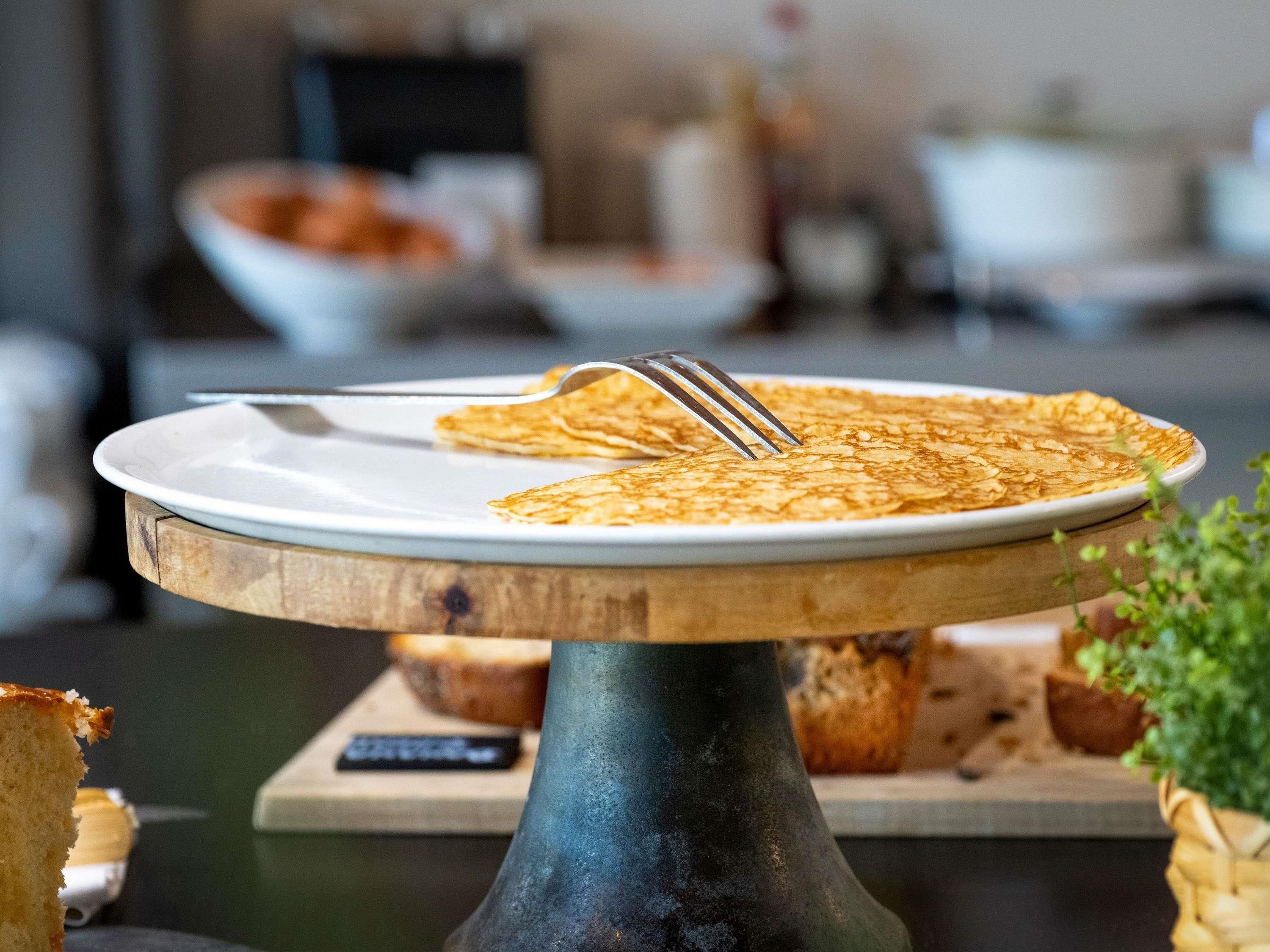 Un plato de crepas sobre un soporte de madera, con un tenedor encima.