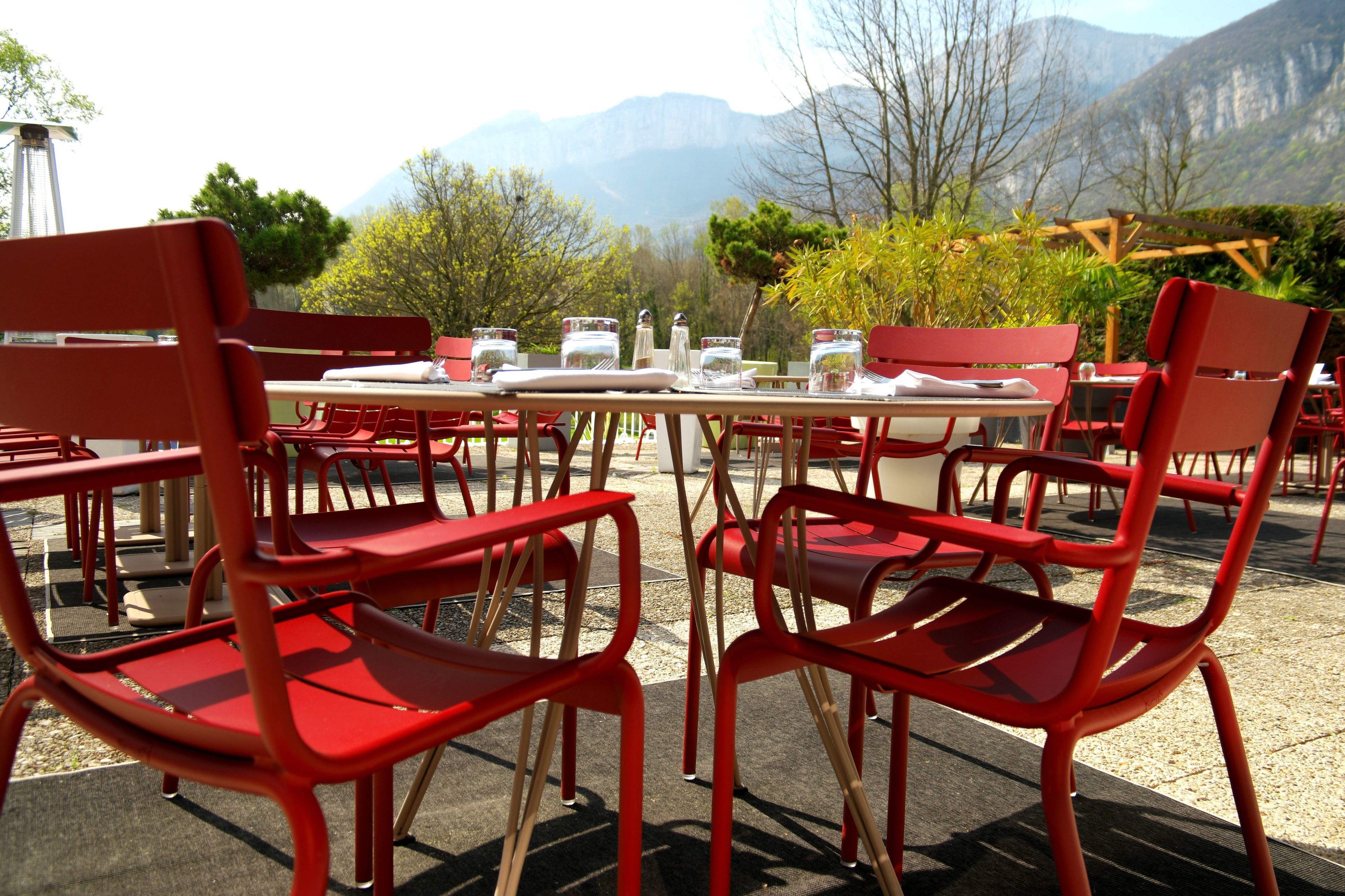 Outdoor dining tables with red chairs, set up in a scenic outdoor area with mountains in the background.