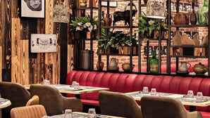 L’intérieur d’un restaurant présente des panneaux muraux en bois, un coin salon avec des banquettes rouges et des étagères remplies de divers objets.