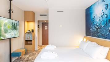 A hotel room with a bed, a TV, a desk with a computer, and a painting on the wall.