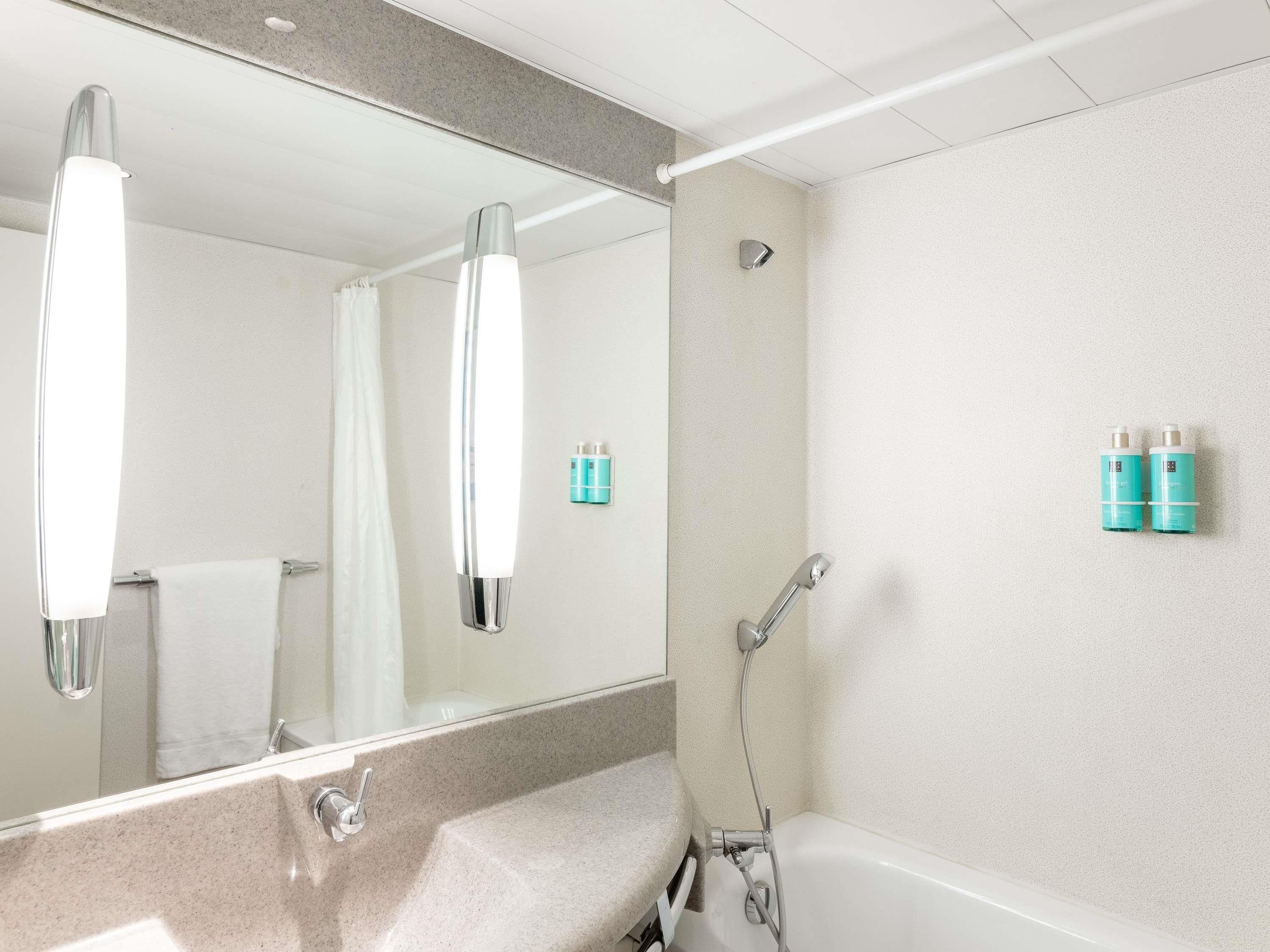 A bathroom with a sink, mirror, shower, and two toiletry bottles on the wall.