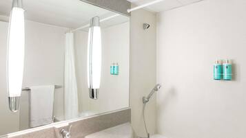 A bathroom with a sink, mirror, shower, and two toiletry bottles on the wall.