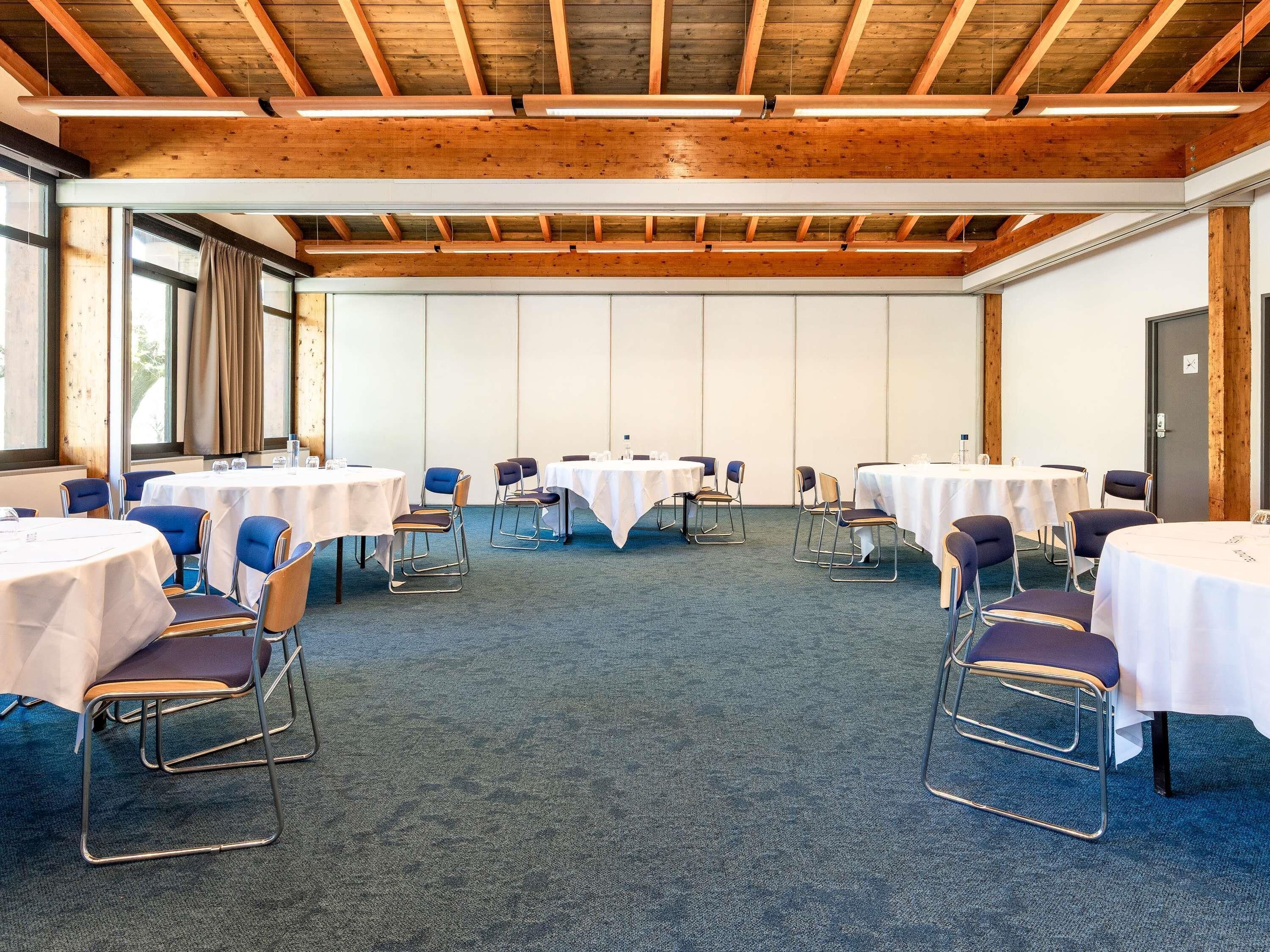 A conference room with round tables, chairs, and a wooden ceiling.