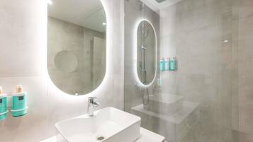 A modern bathroom with a large oval mirror, a rectangular sink, and a glass-enclosed shower.