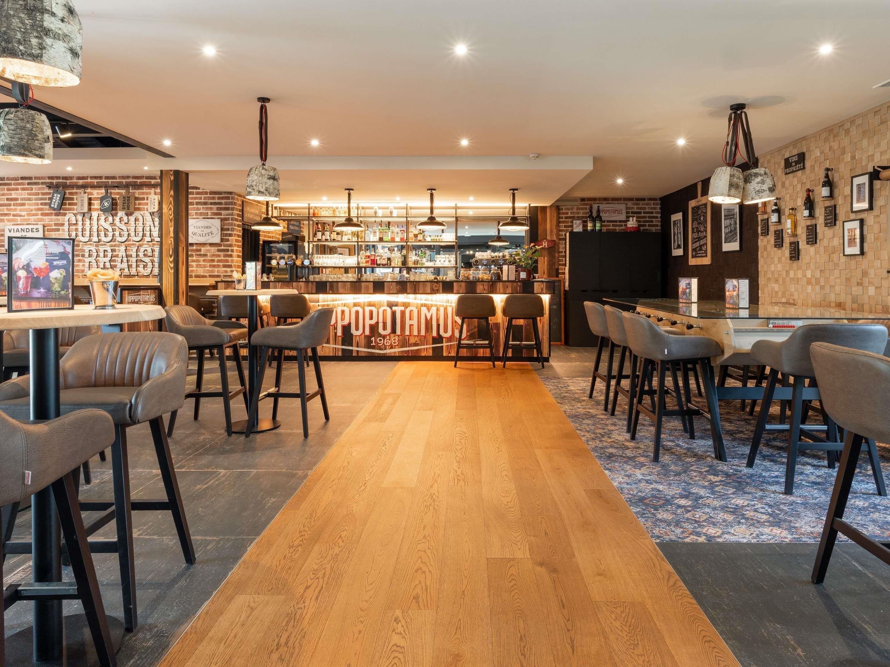 A bar area with a wooden floor, bar stools, and a counter displaying various bottles.