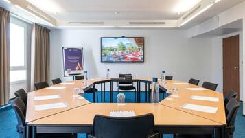 A conference room with a large table, chairs, a screen, and a banner.