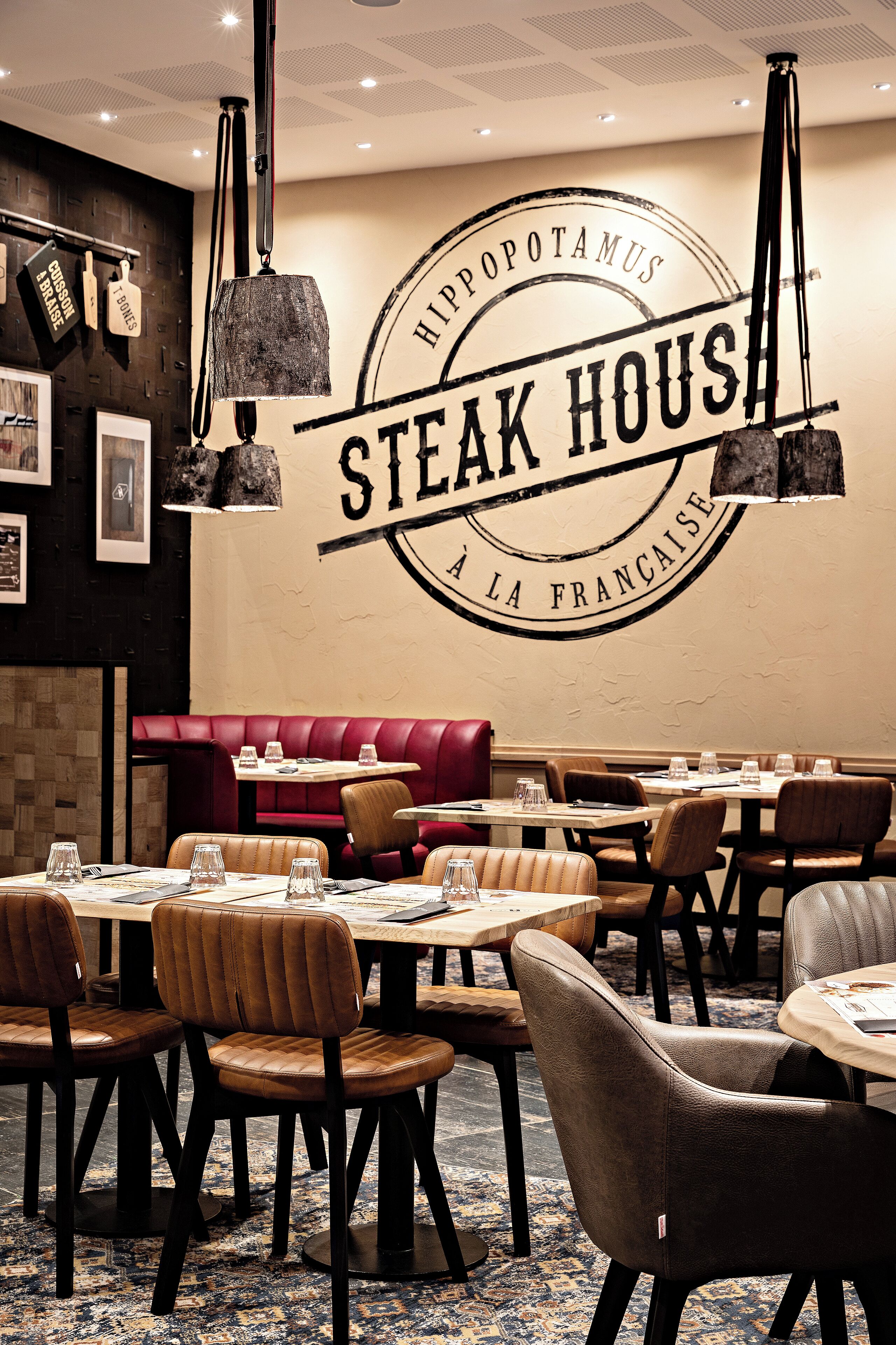 Un interior de restaurante con un letrero llamativo que dice 'STEAK HOUSE', asientos tipo banca de cuero y mesas de madera.