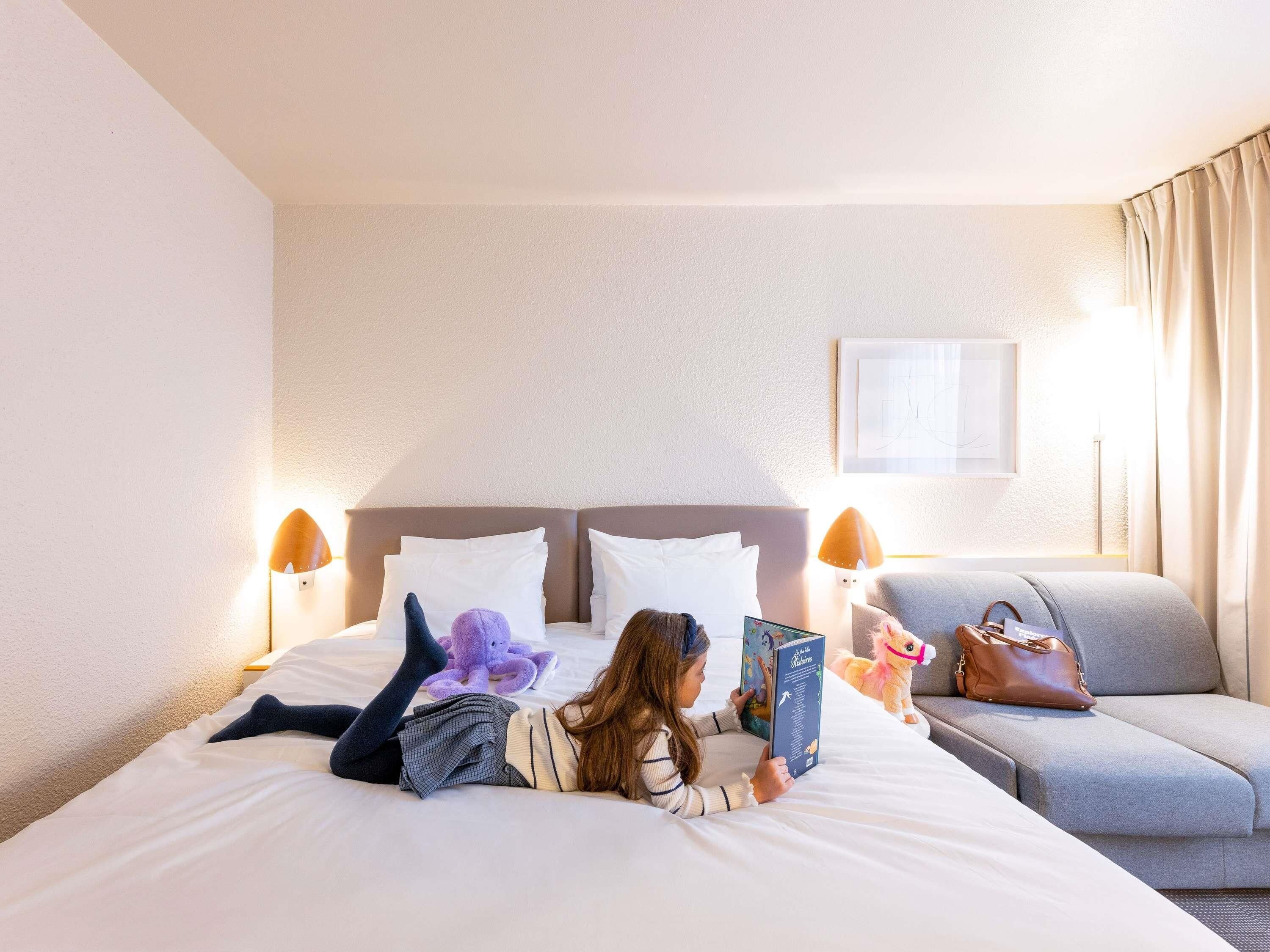 A hotel room with a bed, a sofa, a lamp, and a framed picture on the wall.