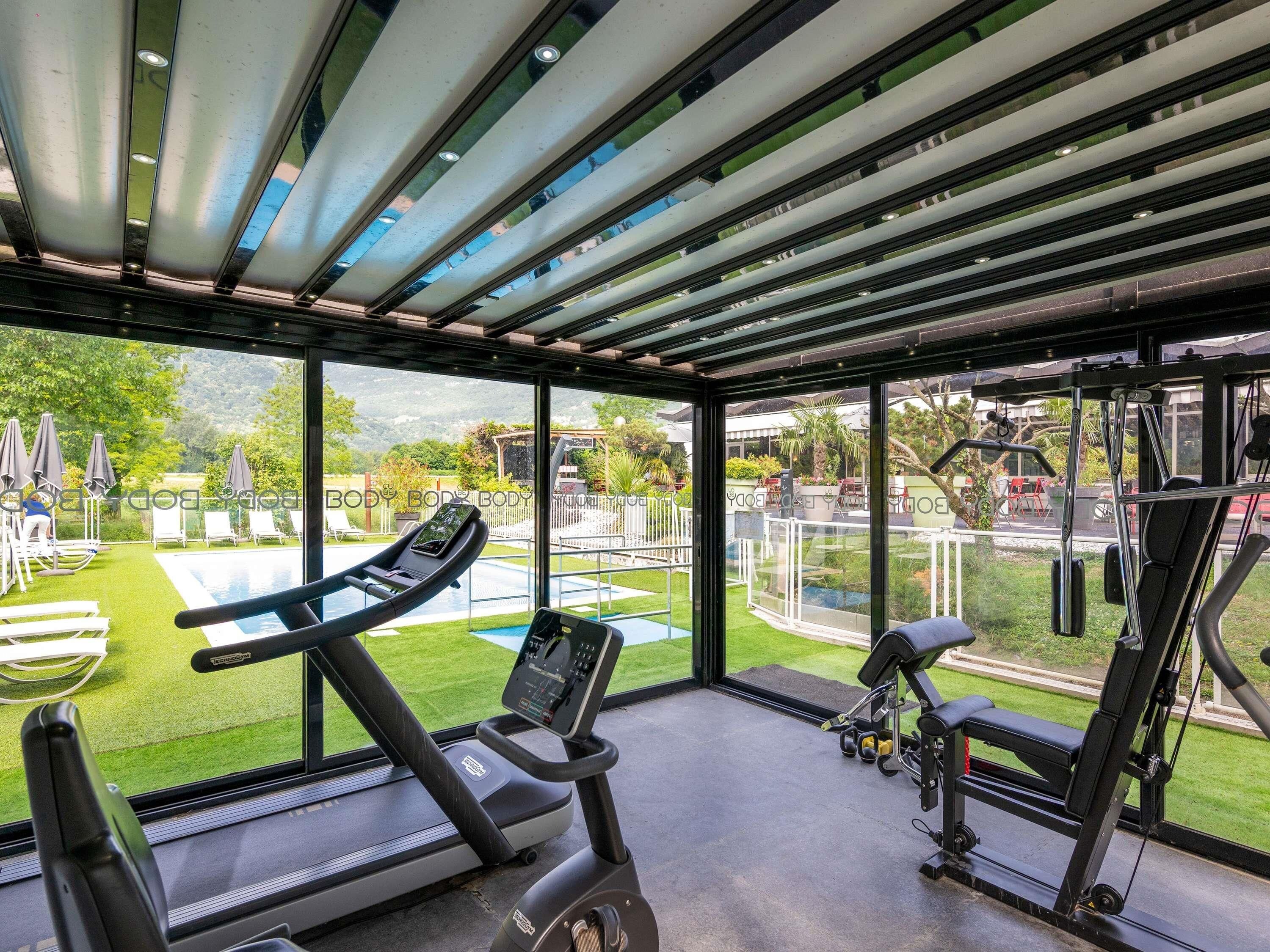 A gym with exercise equipment, a treadmill, and a view of a swimming pool and garden.