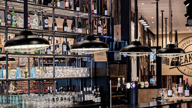 Un espace bar au décor en bois, avec des étagères remplies de bouteilles et de verres, et des luminaires suspendus.