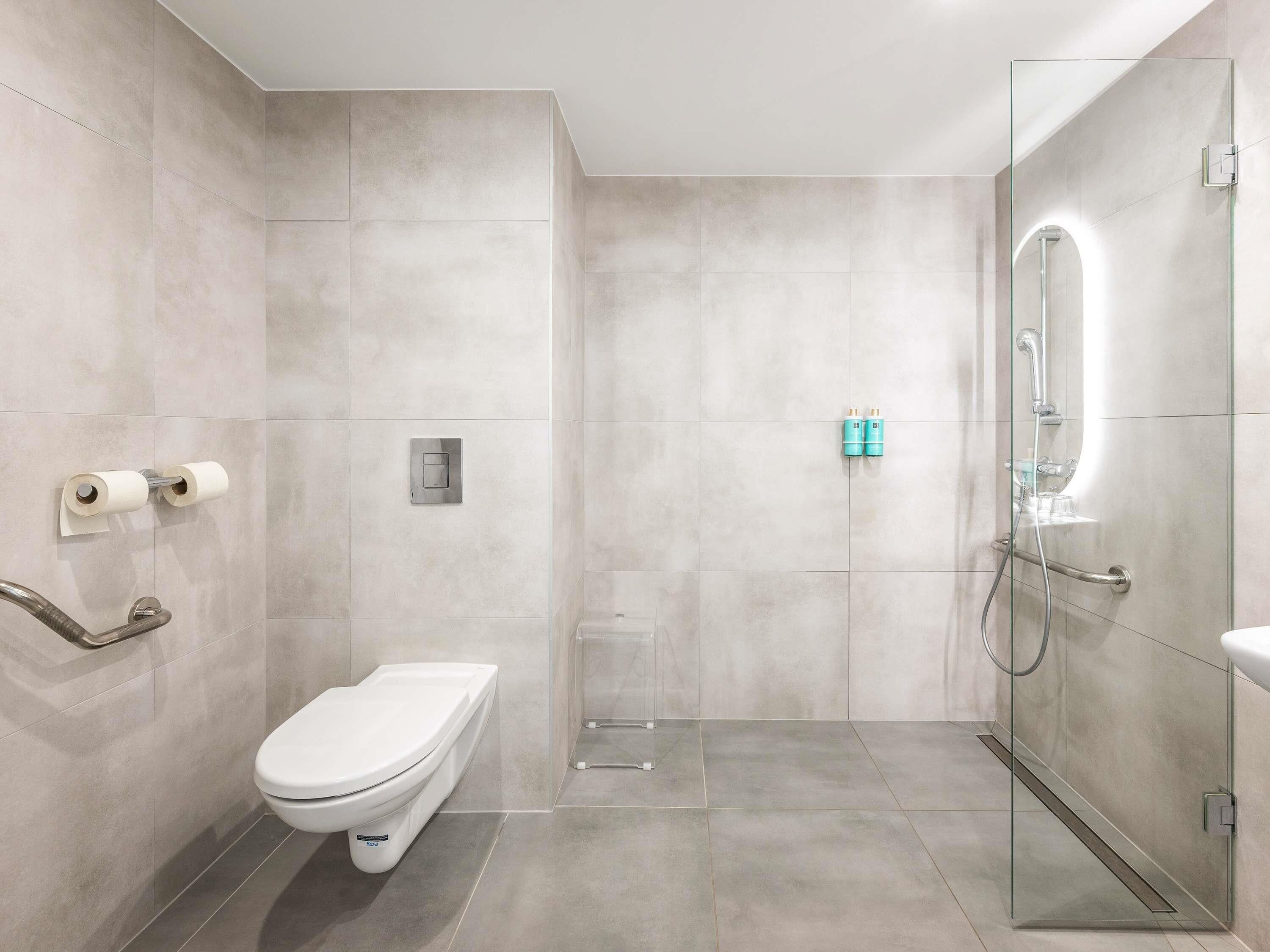 Un baño moderno con inodoro, cabina de ducha de vidrio y barra de apoyo.