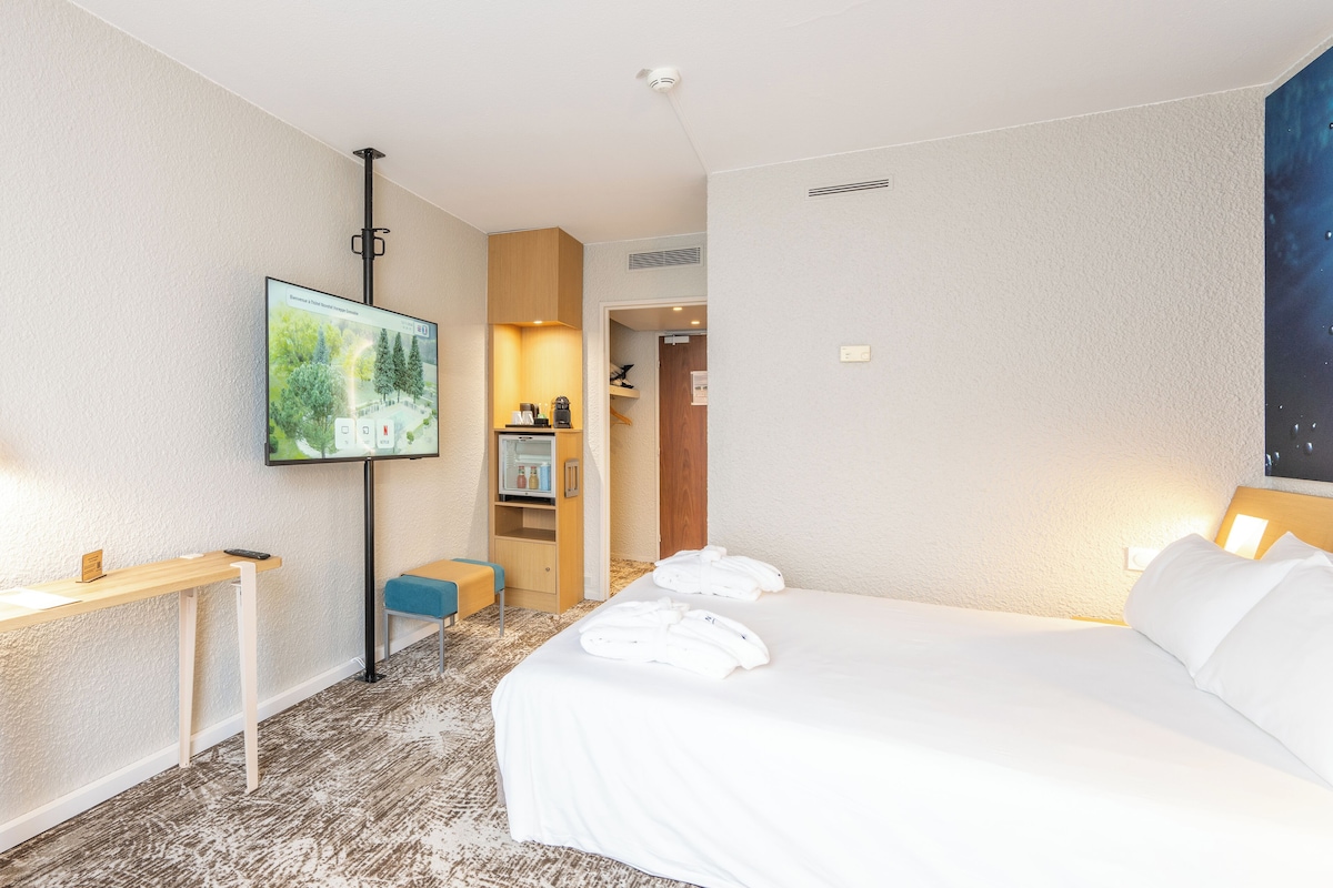 Une chambre d’hôtel avec un lit, un bureau, une télévision et une salle de bain, visibles à travers une porte ouverte.