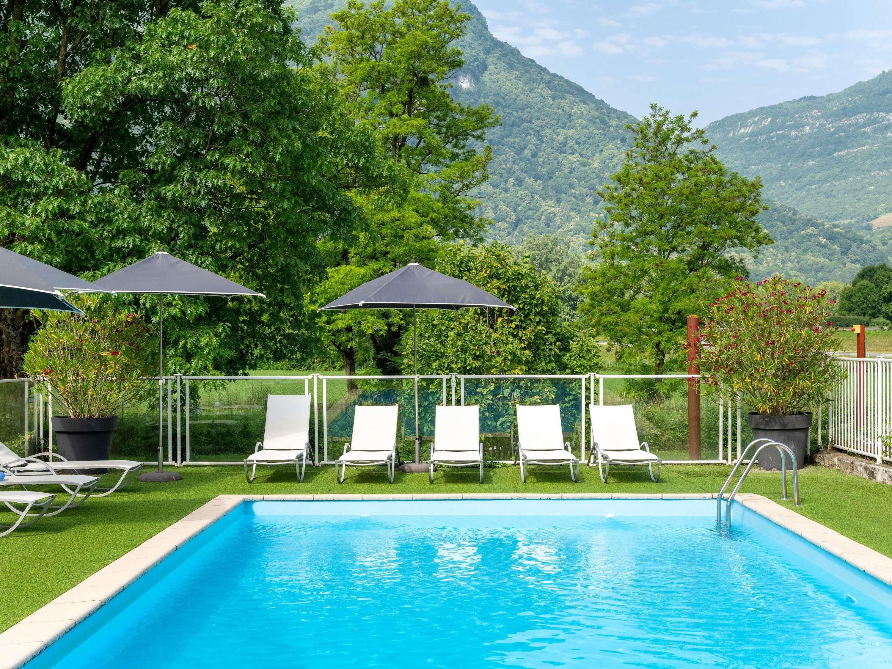 Una piscina con lettini e ombrelloni, circondata da vegetazione e montagne.