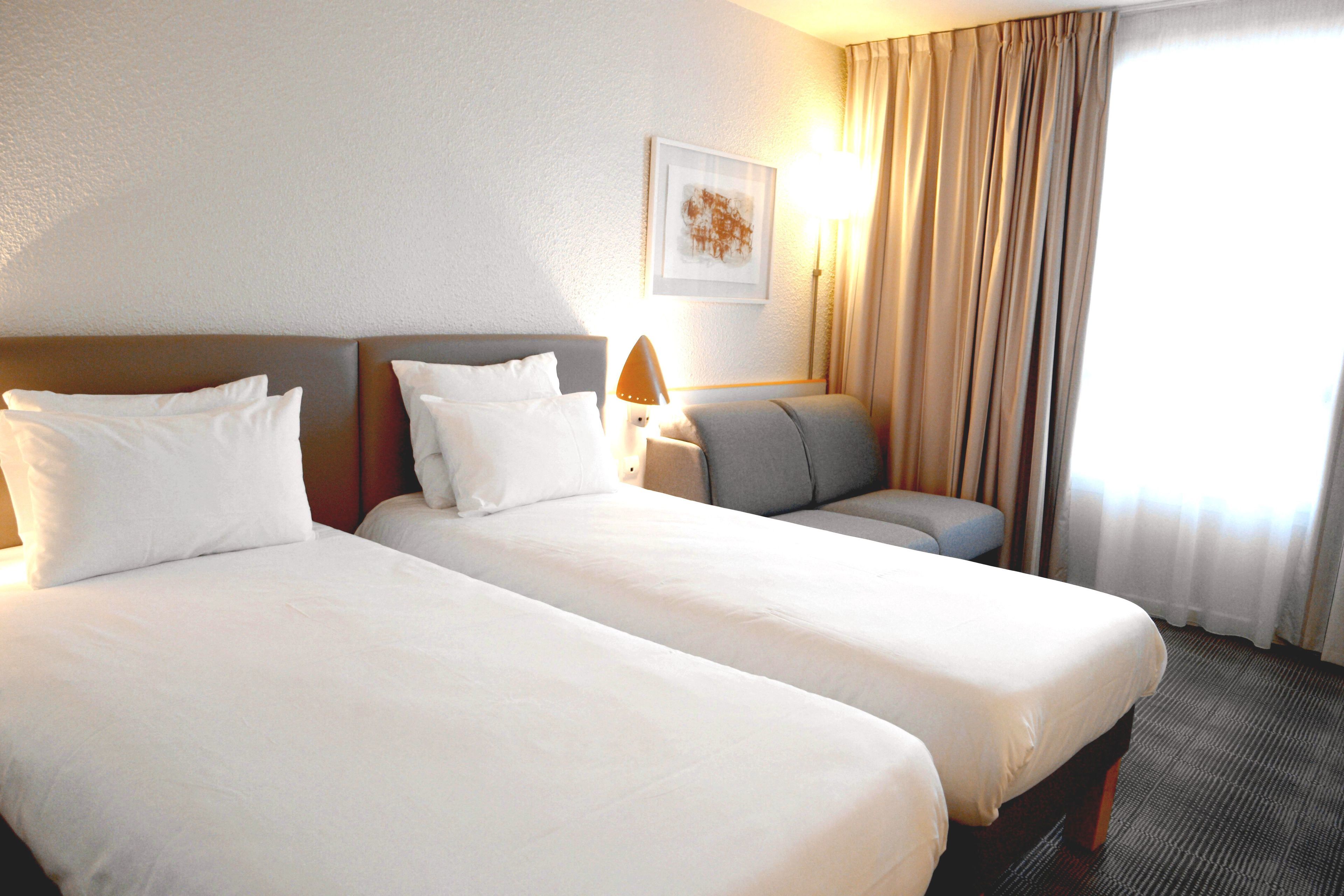 A hotel room with two beds, a sofa, a lamp, and a painting on the wall.