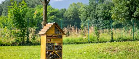 Una casa pájaro de madera con compartimentos para anidar y alimentarse, ubicada en un campo de césped con montañas al fondo.