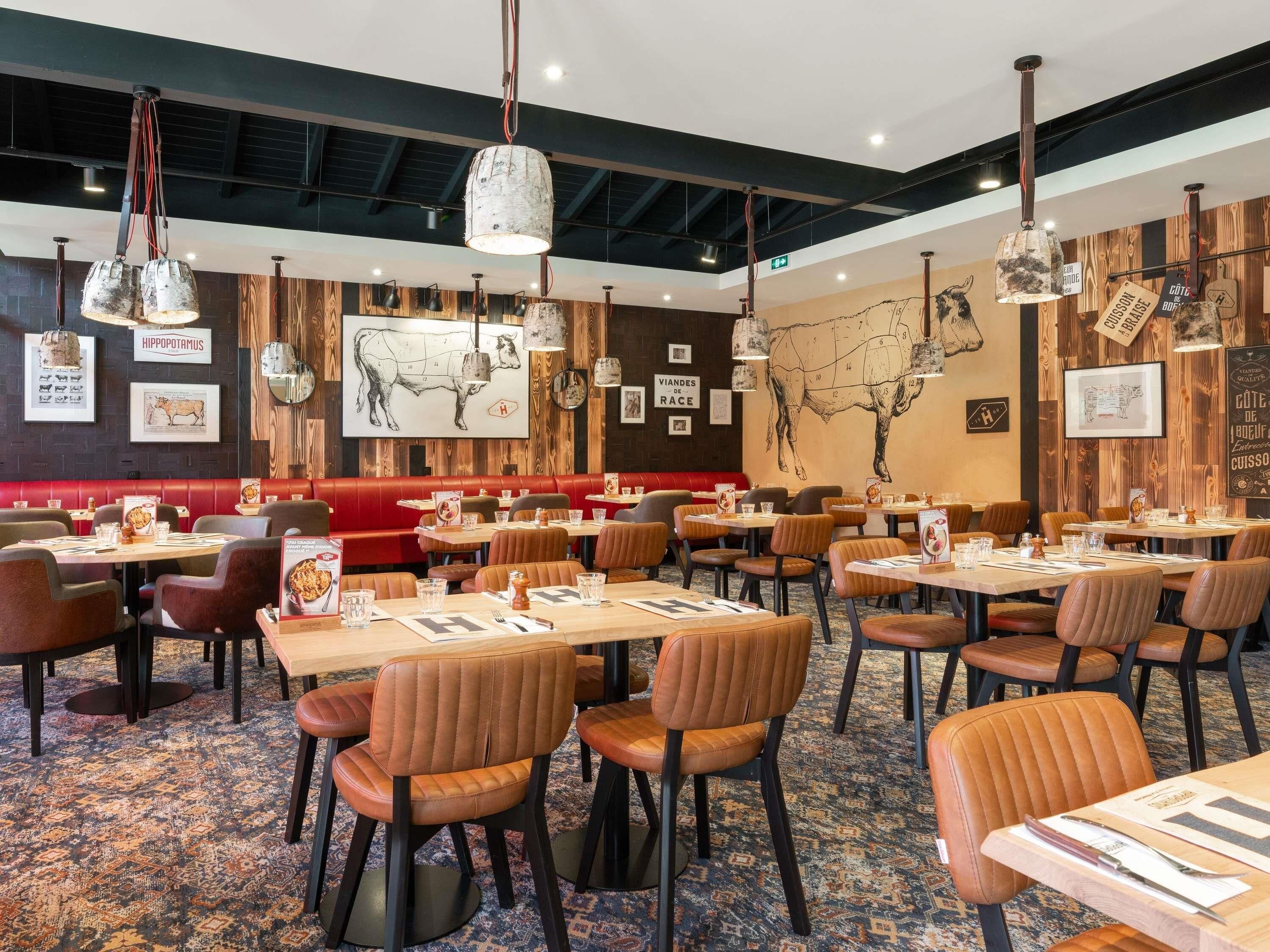 Ein Restaurant mit Sitzecken und Tischen, Wandverkleidung aus Holz und hängenden Pendelleuchten.